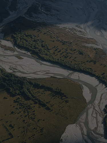 Aerial view of a winding river with patches of greenery and sandbanks, surrounded by natural landscapes.